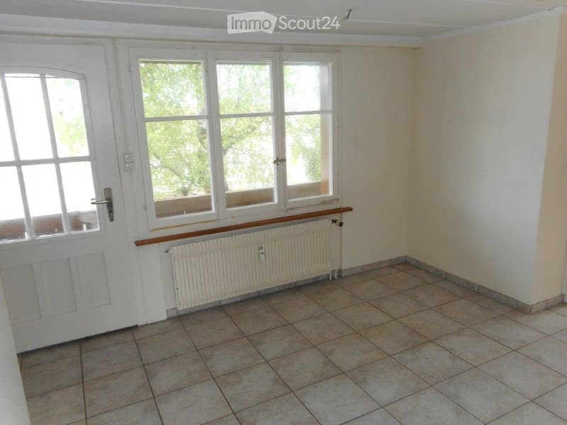 Empty room with tiled floor, white walls, large windows, and a radiator below the windows.