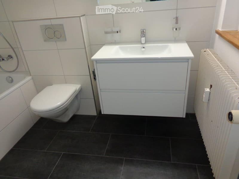 Modern bathroom with white tiles, black floor tiles, a toilet, a sink with a faucet, and a radiator.
