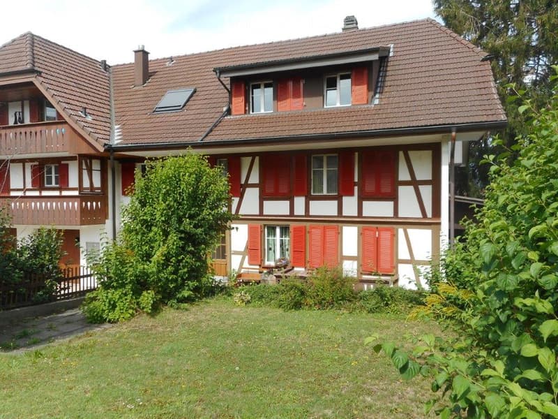 Two-story house with red-tiled roof, white and brown facade, red shutters, and a balcony on the upper floor.