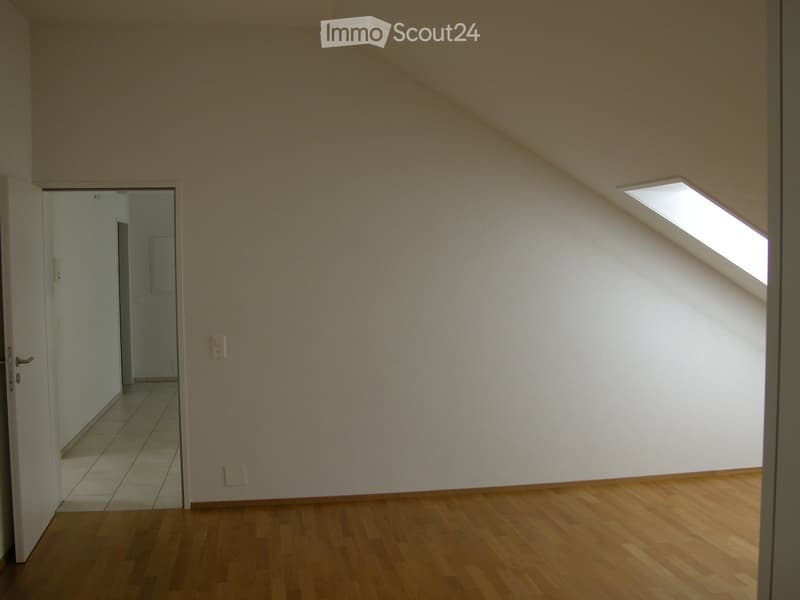 Empty room with wooden flooring, white walls, and a skylight window. A doorway leads to another tiled area.