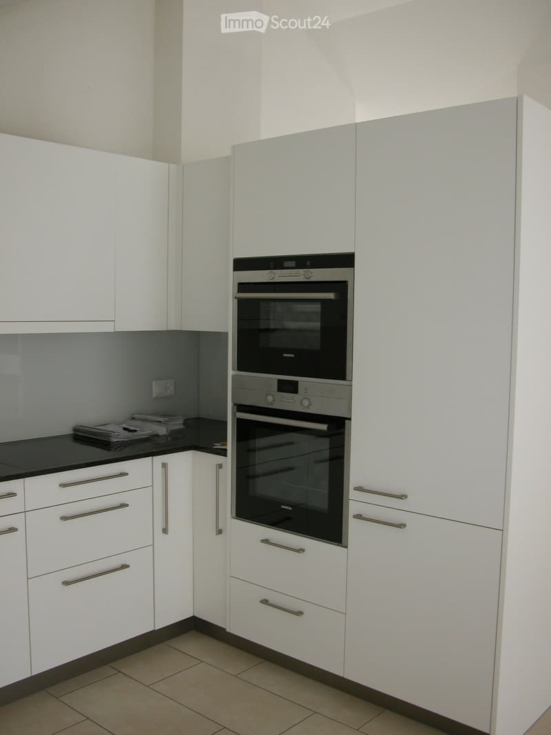 Modern kitchen with white cabinets, stainless steel oven, and tiled floor.