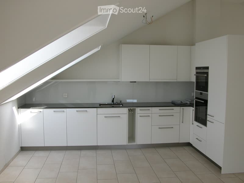 Modern kitchen with white cabinets, tiled floor, and built-in appliances including a sink and oven. The space features large windows and ample storage.