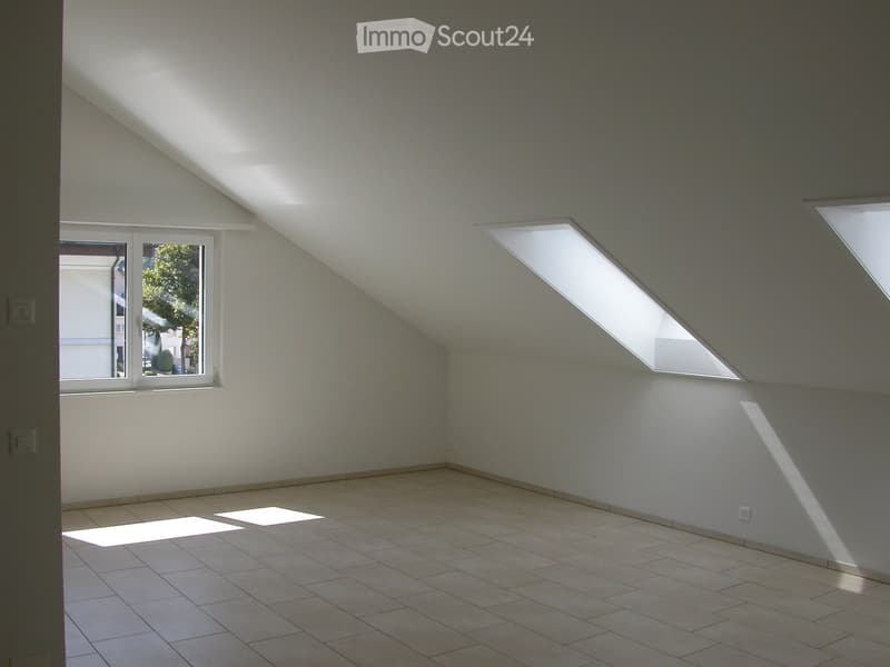 Empty attic room with slanted ceilings, tiled floor, and multiple skylights allowing natural light to enter.