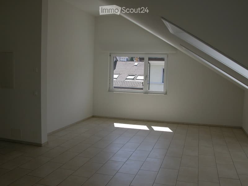 Empty attic room with tiled floor, white walls, and skylight windows allowing natural light to enter.
