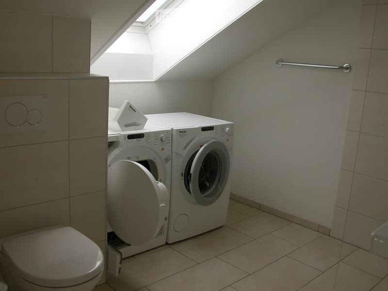Modern bathroom with a toilet, washing machine, and dryer, featuring tiled walls and a skylight window.