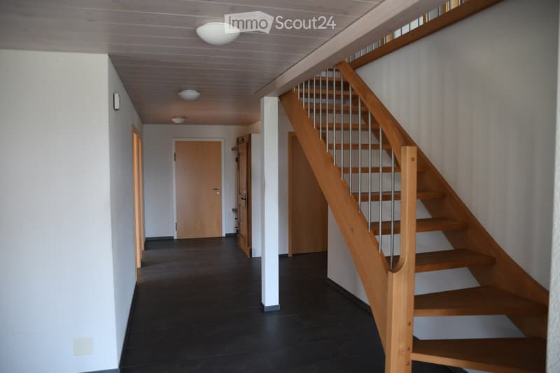 Modern hallway with wooden staircase, dark tiled floor, white walls, and recessed lighting.