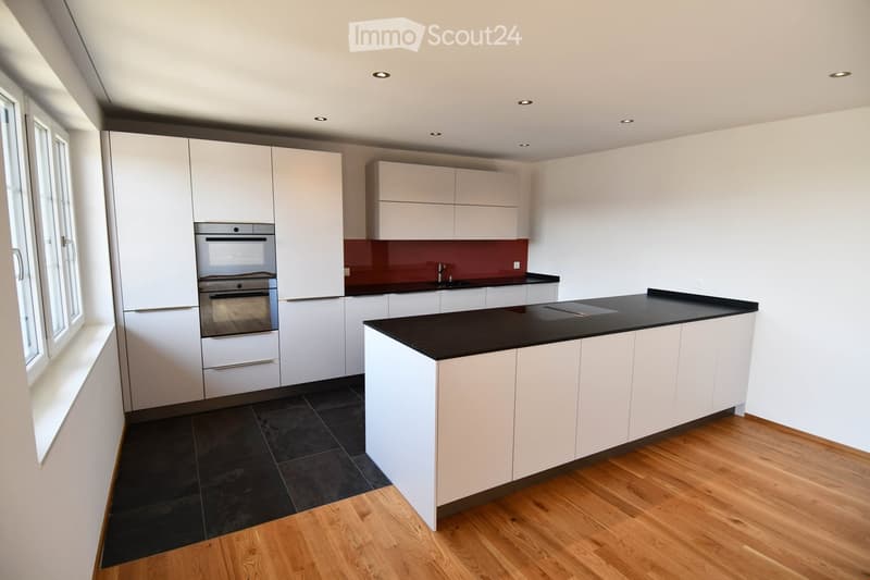 Modern kitchen with white cabinets, black countertop, stainless steel oven, and a dark backsplash.