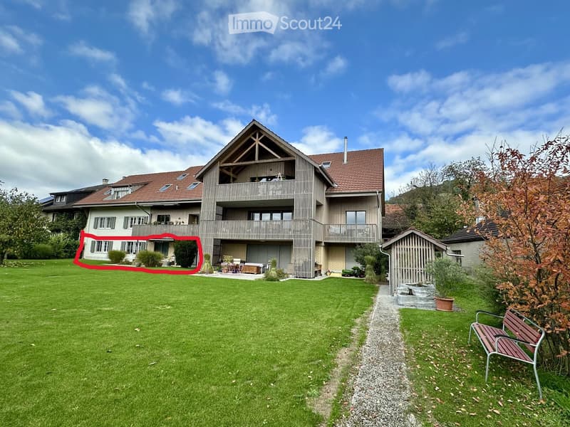 Two-story house with a red-tiled roof, multiple windows, and a balcony. The house is surrounded by a well-maintained lawn and garden area.