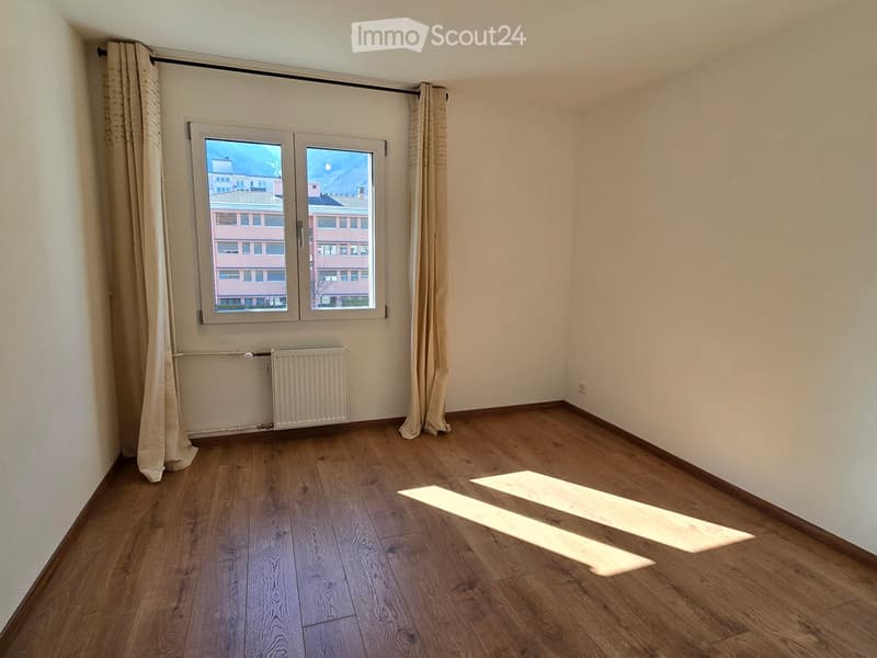 Empty room with wooden flooring, white walls, and a window with curtains. A radiator is visible below the window.