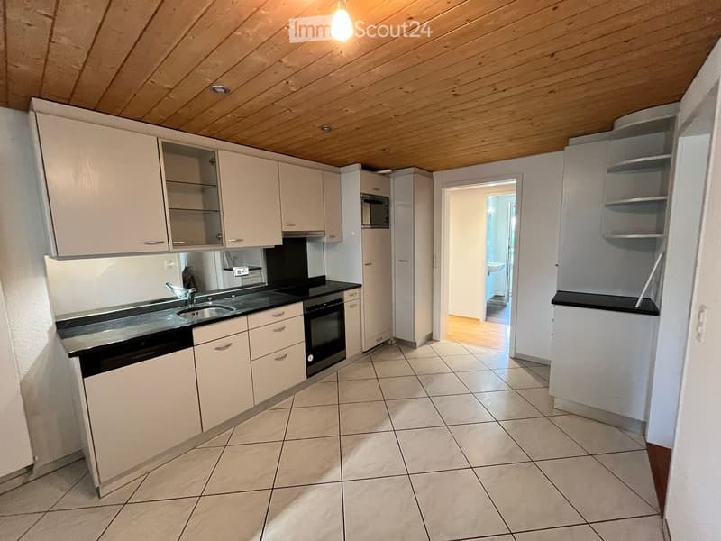 Modern kitchen with white cabinets, black countertops, and stainless steel appliances, including a sink, oven, and microwave. The space features tiled flooring and an open doorway leading to another room.