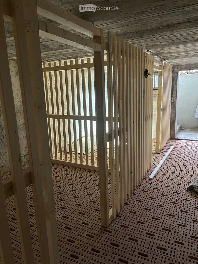 Empty room with exposed wooden beams, a wooden partition, and a perforated floor grid. No furniture or equipment is present.