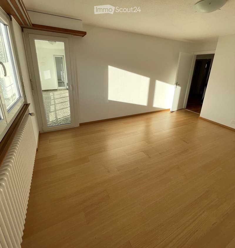 Empty room with wooden flooring, white walls, large window, and sliding glass door leading to another space.