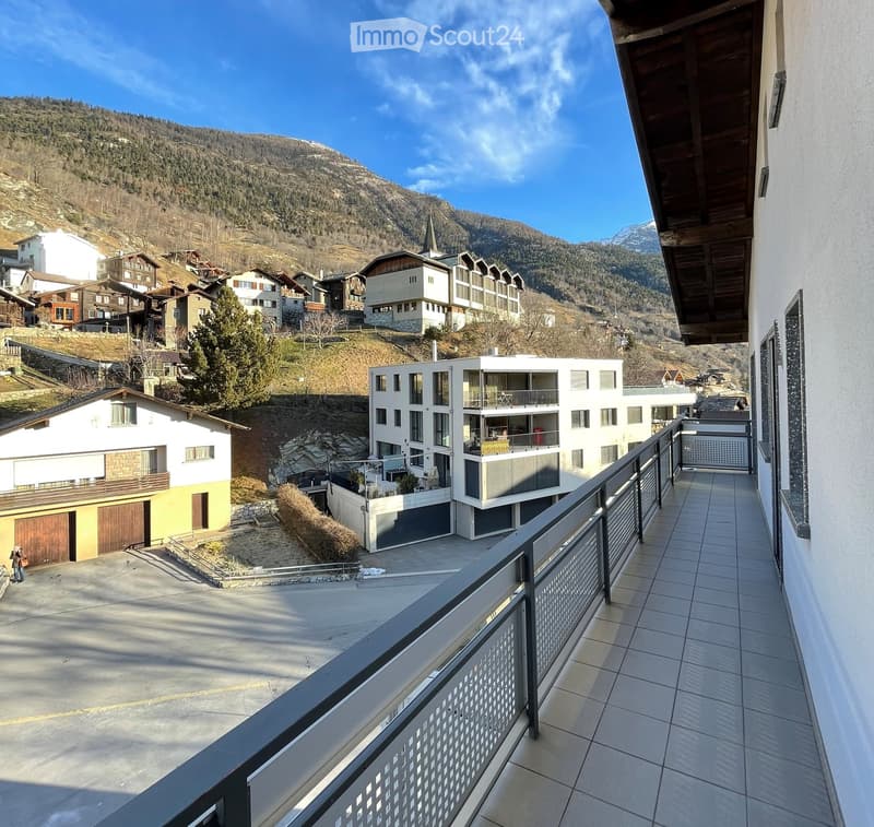 Balcony overlooking a scenic mountain village with houses, a garage, and a clear blue sky.