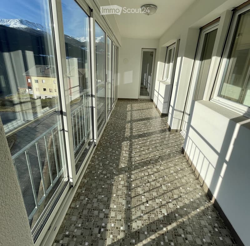 Balcony with tiled floor, large windows, and a view of mountains and buildings.