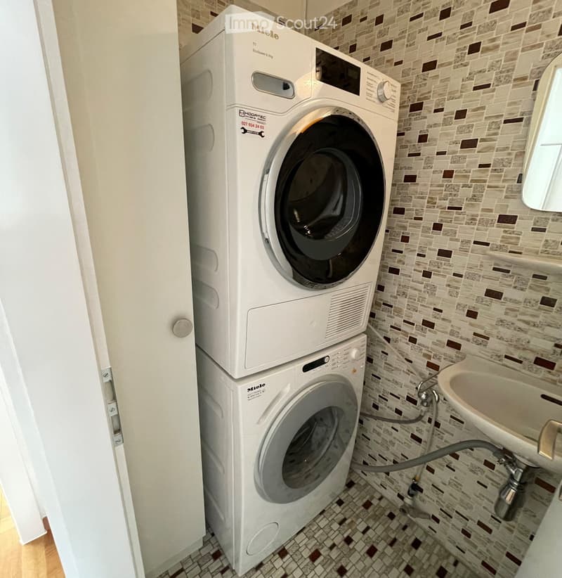 Bathroom with a washing machine and a sink, featuring tiled walls and a small window.