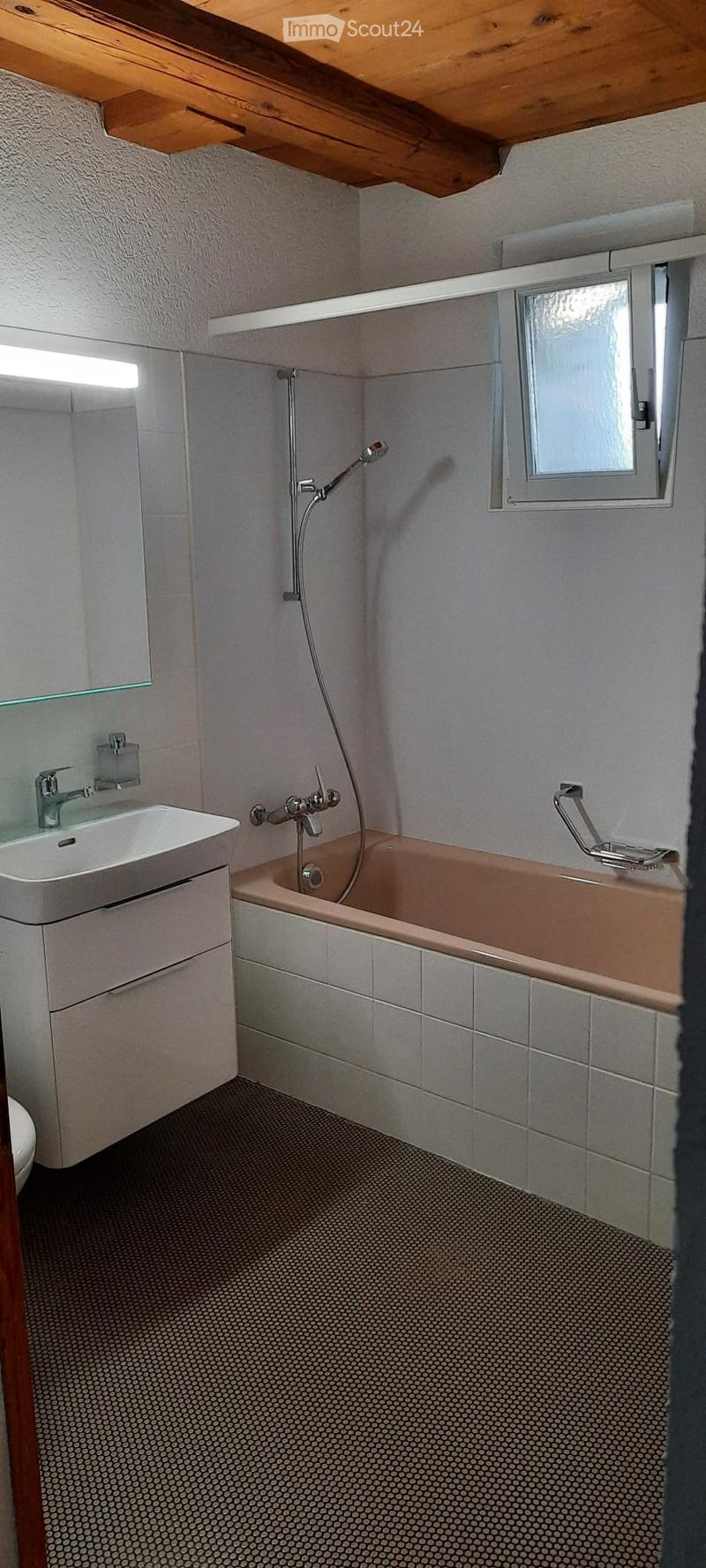 Modern bathroom with a bathtub, sink, and mirror. Features a wooden ceiling and a window with frosted glass.