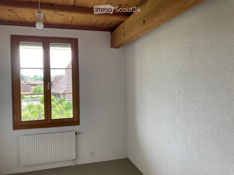 Unfurnished Room. Empty room with white walls, wooden ceiling beams, large window with wooden frame, radiator, and visible outdoor view.