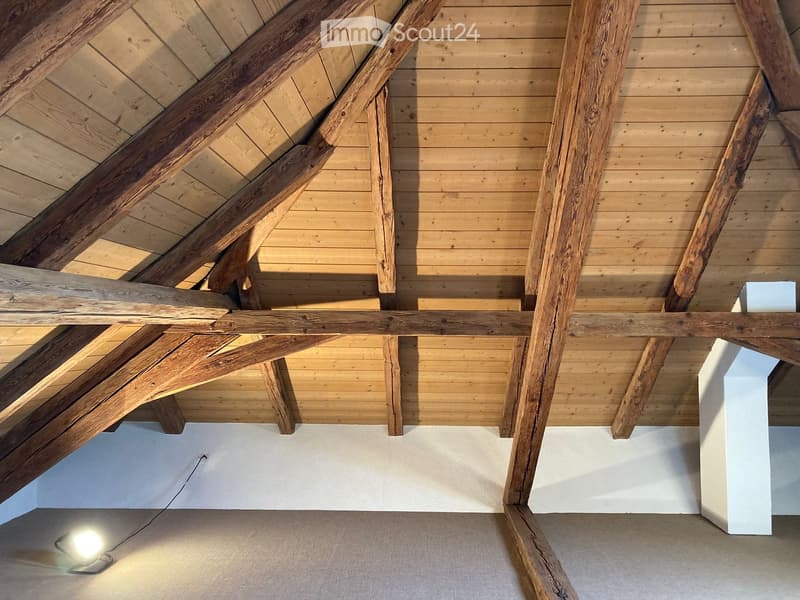 Unfurnished Room. Exposed wooden beams and herringbone wooden flooring in an attic space with white walls and a single light fixture.
