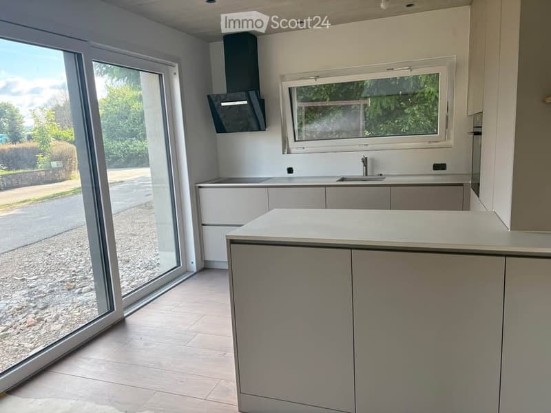 Modern kitchen with white cabinets, a central island, and large windows offering a view of the outdoors.