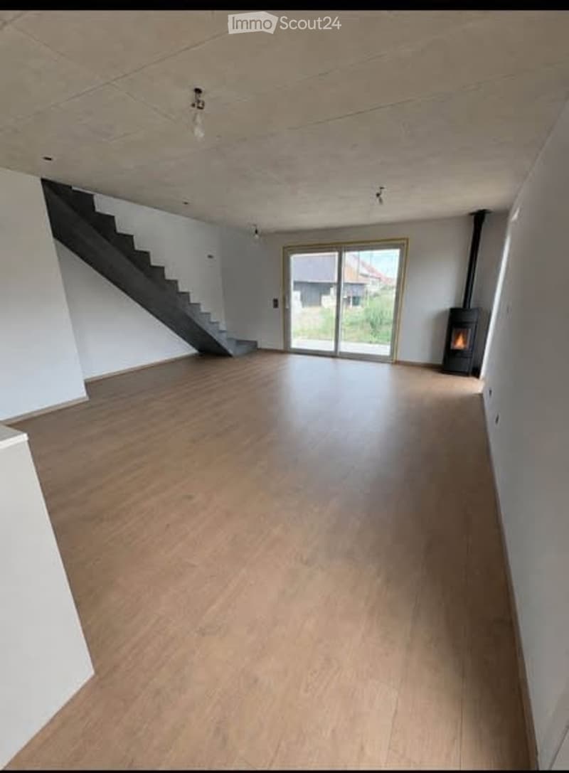 Empty room with wooden flooring, white walls, staircase leading to an upper level, large glass sliding door leading to an outdoor area, and a fireplace in the corner.