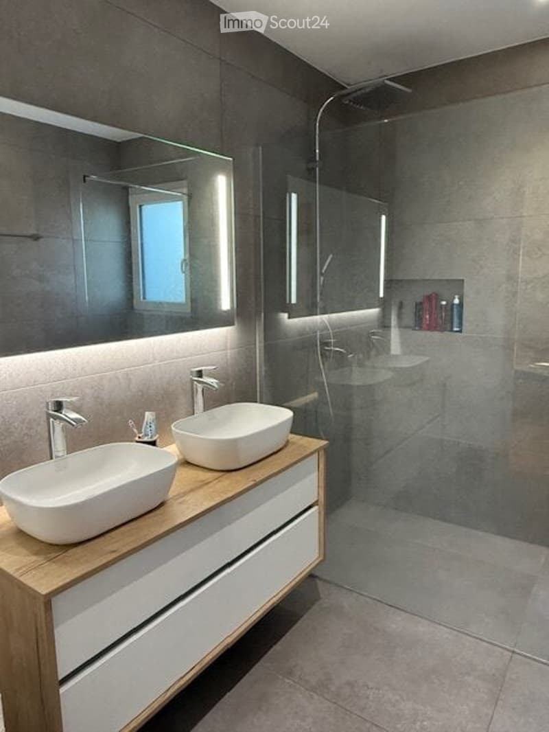 Modern bathroom with double sinks, sleek wooden vanity, large mirror, and a glass-enclosed shower area.