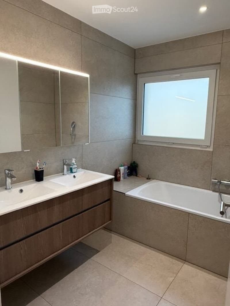 Modern bathroom with double sink vanity, large mirror, bathtub, and a window for natural light.