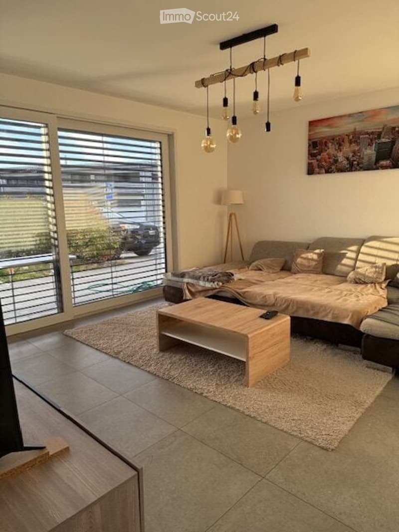 Modern living room with large windows, a sofa, coffee table, floor lamp, and artwork on the wall.