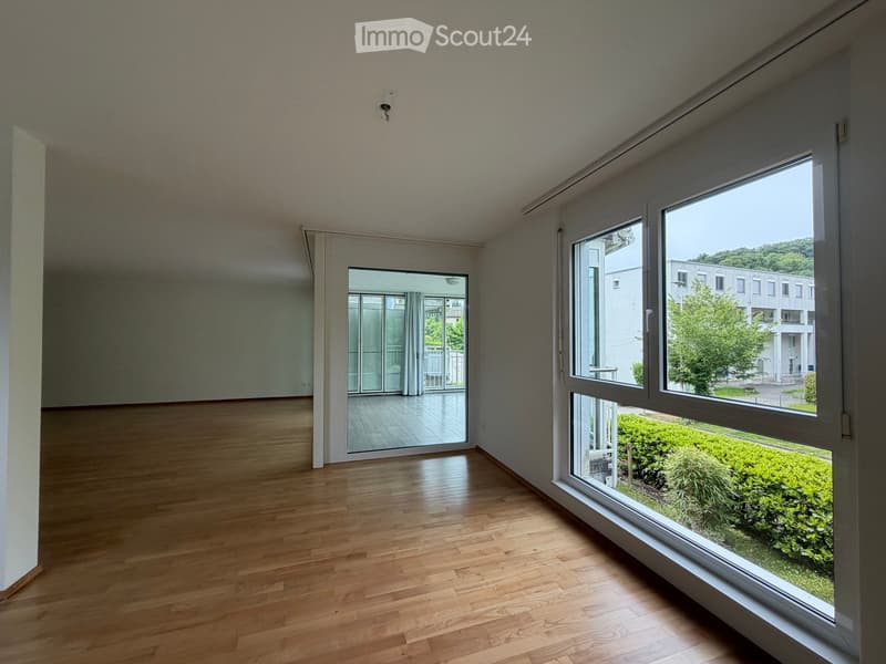 Empty room with wooden flooring, large windows, and a sliding glass door leading to a balcony area.