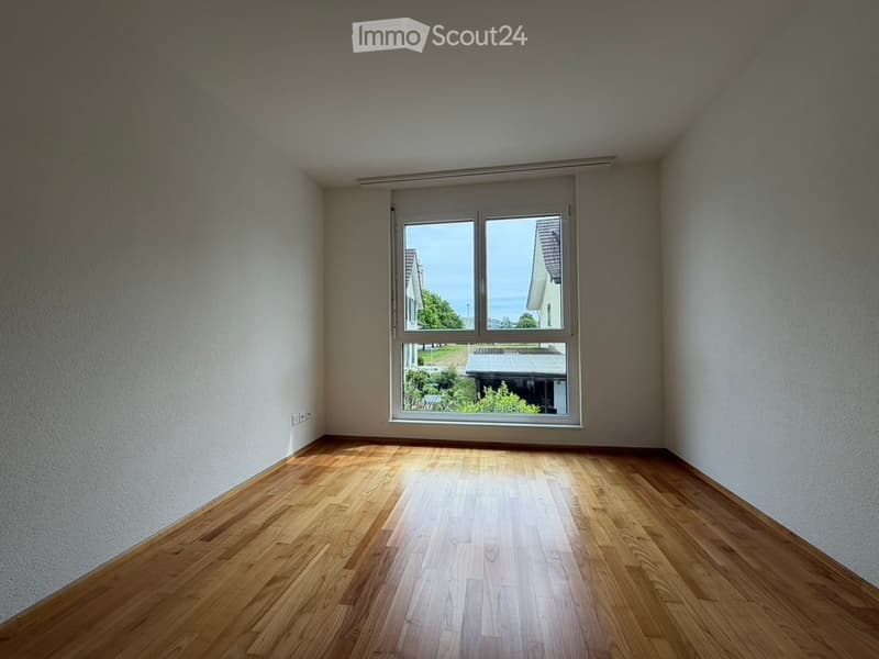 Empty room with wooden flooring and large window offering a view of the outside area.