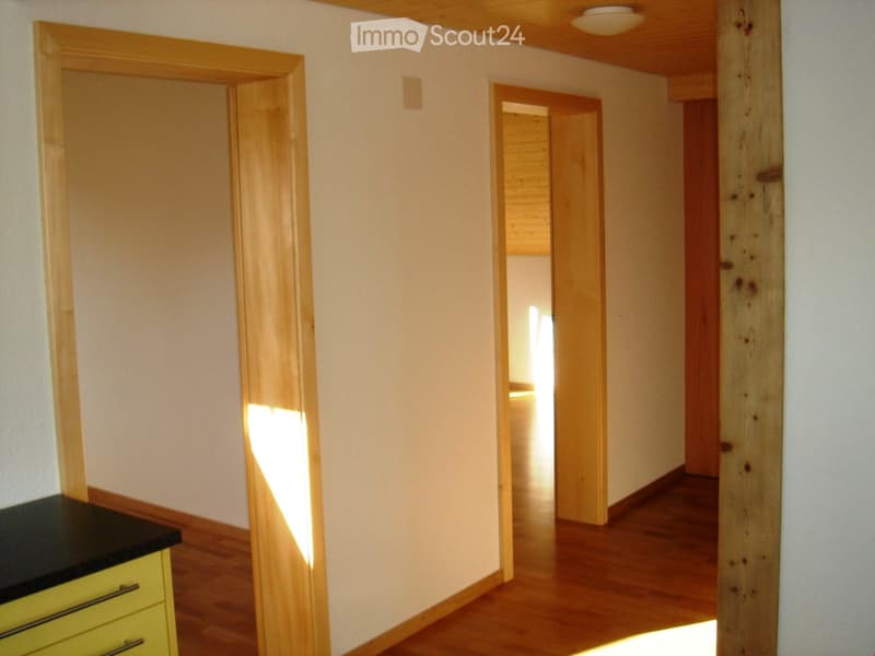 A narrow hallway with wooden flooring and light-colored walls, featuring two open doorways leading to adjacent rooms.