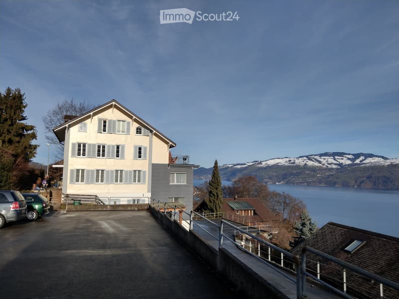 Two-story house with light-colored walls, multiple windows, and a view of a lake and mountains in the background.