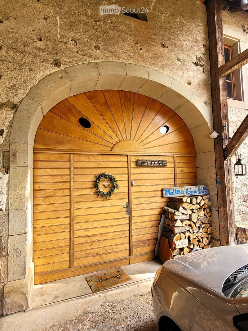 Wooden garage door with a decorative wreath, a stack of firewood, and a car parked nearby.
