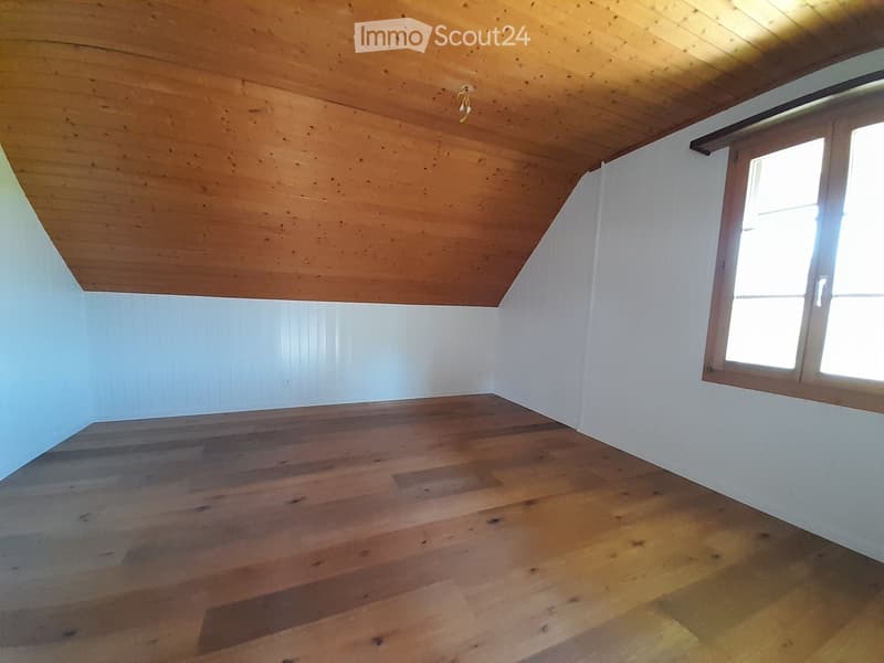 Empty room with wooden floor, white walls, and wooden ceiling. A single window allows natural light to enter.