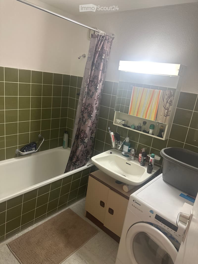 Bathroom with green tiled walls, bathtub, sink, mirror, cabinet, washing machine, and a shower curtain.