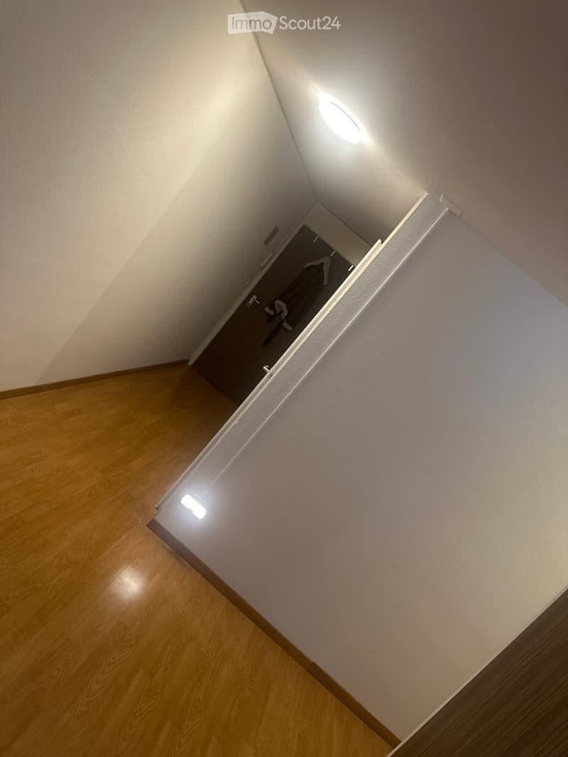 A narrow hallway with wooden flooring and white walls, featuring recessed lighting and an open closet door showing some clothing items inside.