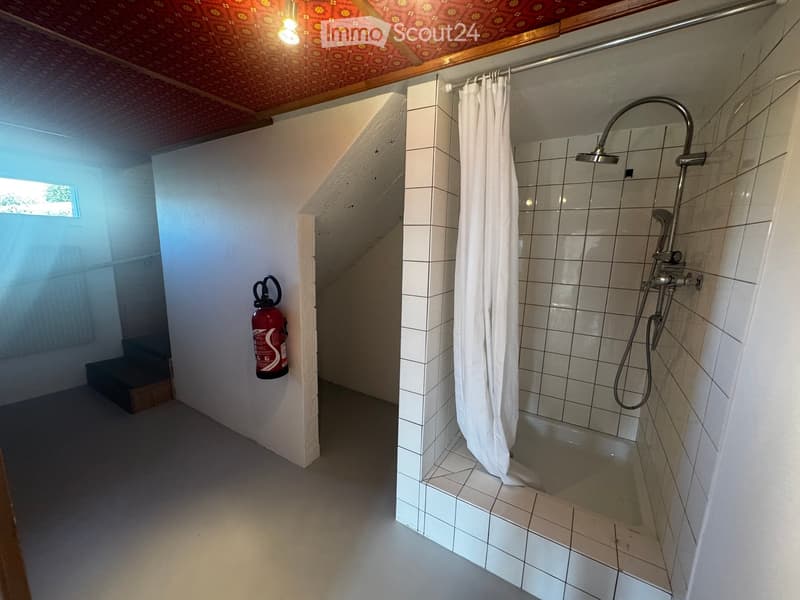 Bathroom. Bathroom with a bathtub, showerhead, and a white shower curtain. A fire extinguisher is mounted on the wall. The ceiling has a patterned design.