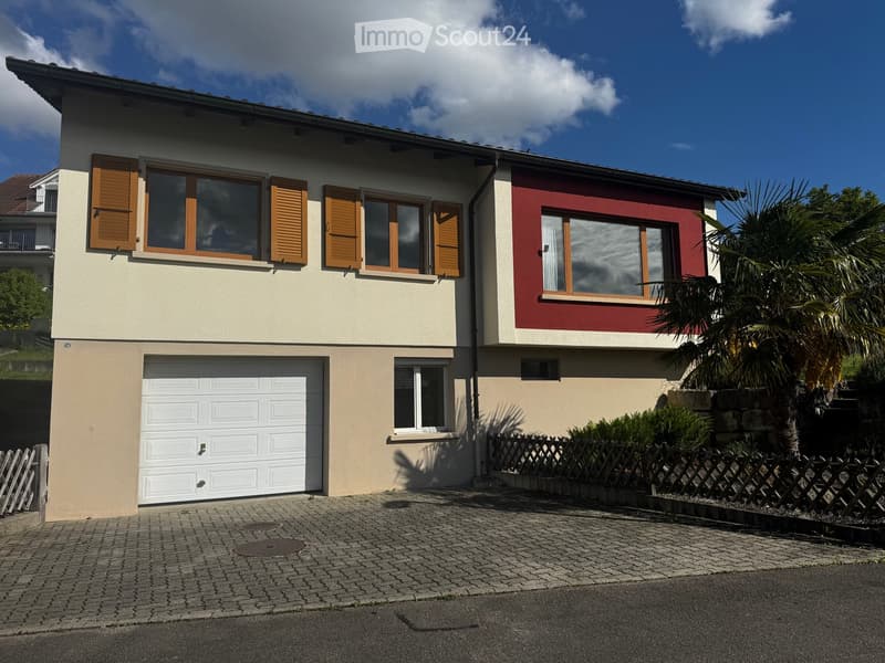 House. Two-story house with beige and red exterior, white garage door, multiple windows with wooden shutters, and a small garden area with a palm tree and wooden fence.