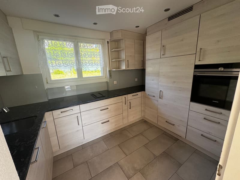 Kitchen. Modern kitchen with light wood cabinets, black granite countertops, and a built-in oven. Features a window with decorative blinds and tiled flooring.