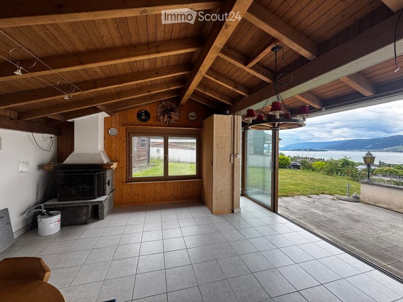 Furnished Room. Bright living room with wooden beams, fireplace, large windows, and a view of the lake and mountains.