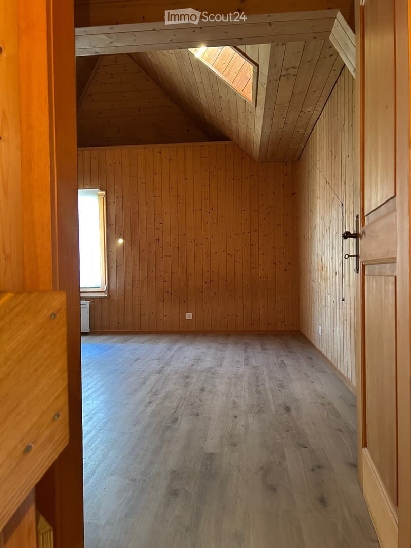 Empty wooden hallway with exposed wooden beams and a skylight, featuring a polished wooden floor and natural light from a window at the end.
