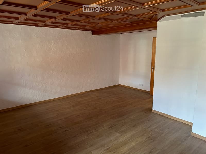 Empty room with wooden flooring, white walls, and a wooden door. The ceiling features a decorative wooden panel design.