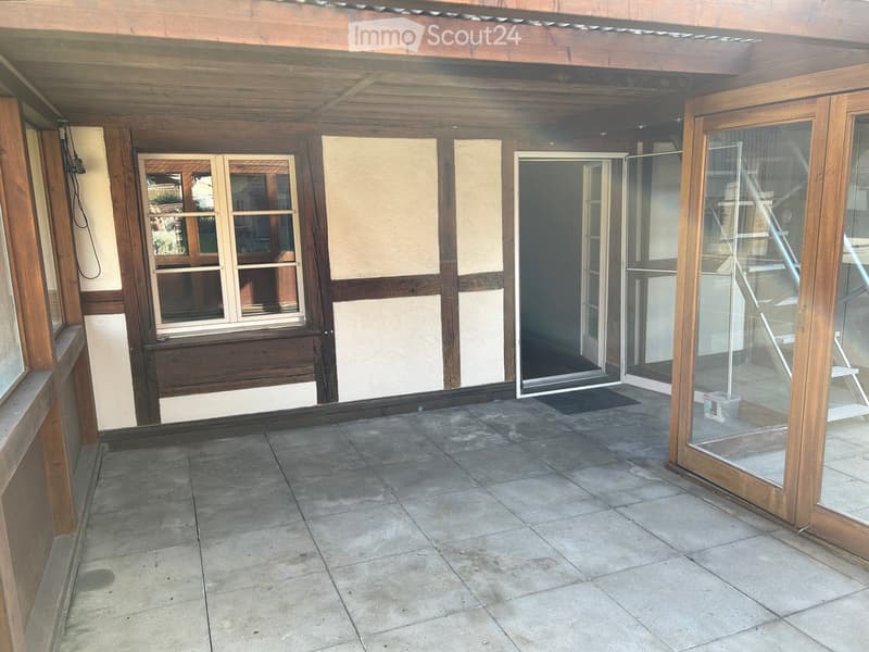 Wooden-framed balcony with tiled floor, large windows, and sliding glass doors leading to the interior.