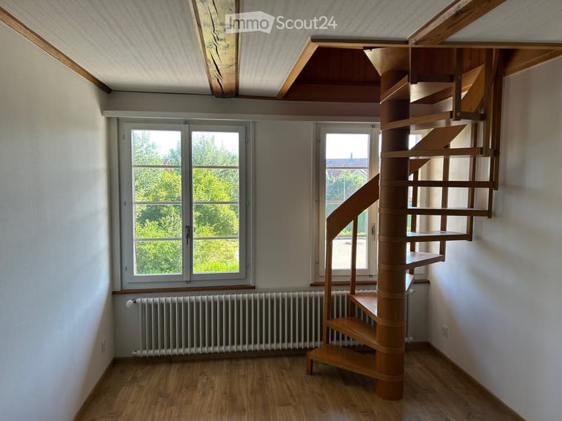 Spacious hallway with wooden floor, white walls, large windows, and a modern wooden spiral staircase leading upwards.