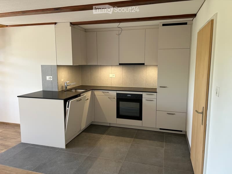 Modern kitchen with light-colored cabinets, a black countertop, a sink with a faucet, and an oven. The floor is tiled, and the walls are painted in a neutral tone.