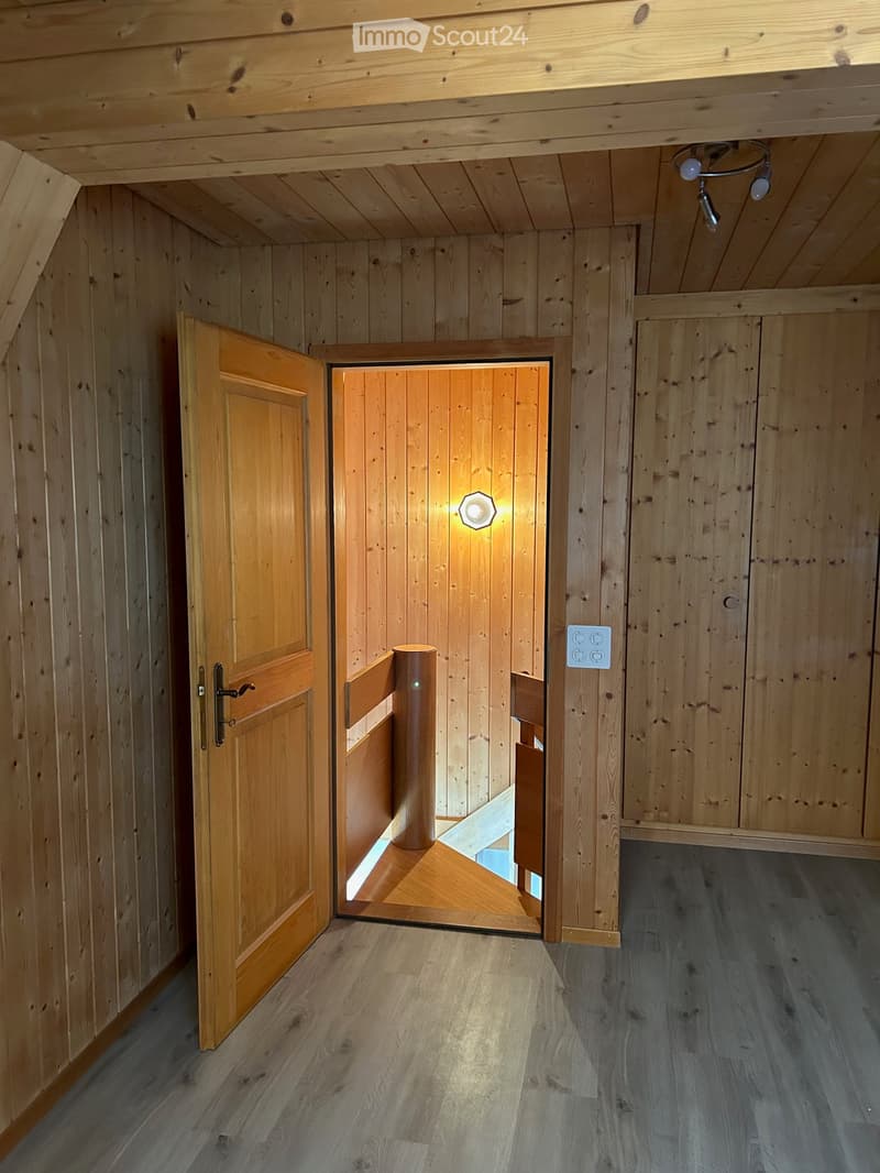 Wooden-paneled hallway with a wooden door leading to another room, featuring a recessed ceiling light and a visible light switch.