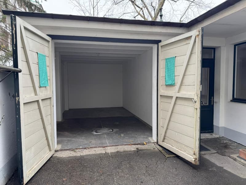 Empty, large white garage, white walls, grey floor, two wooden doors