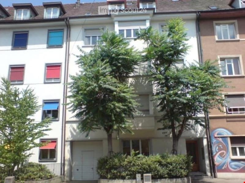 6 story white apartment building with trees and bushes in front, white garage door, red awnings, brown facade on the right side, graffiti on the right building