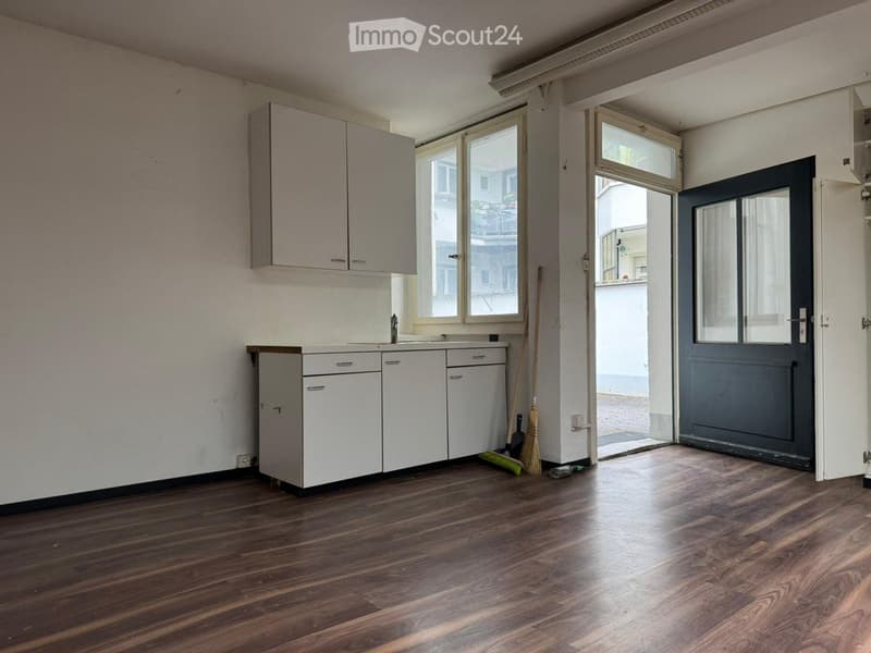 Empty kitchen with white cabinets, wooden floor, windows, a black entrance door.
