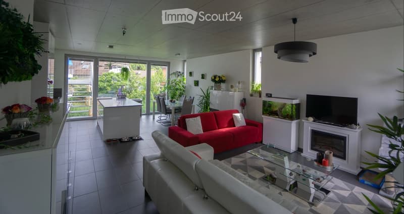 Modern living room with a red sofa, glass coffee table, fireplace, fish tank, and a kitchen island visible in the background.