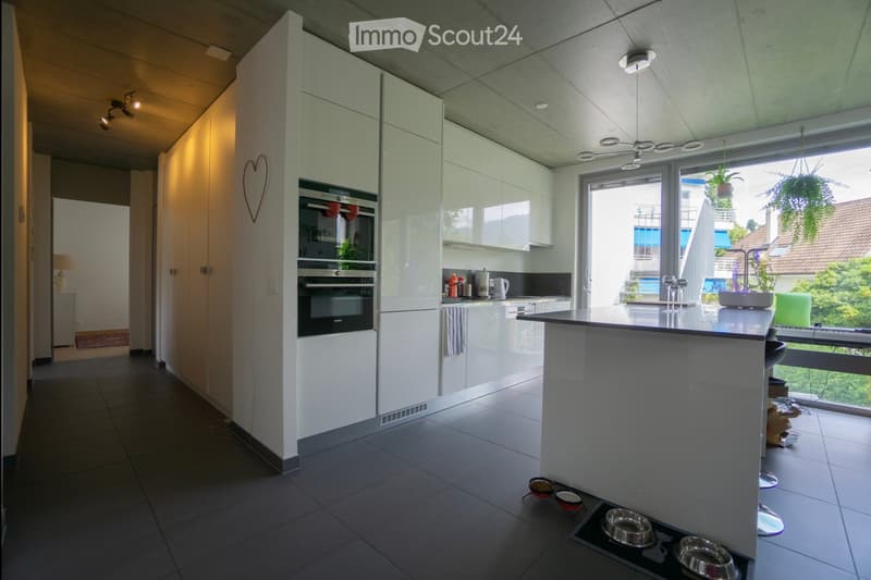 Modern kitchen with white cabinetry, stainless steel appliances, a central island, and a large window overlooking a balcony area.